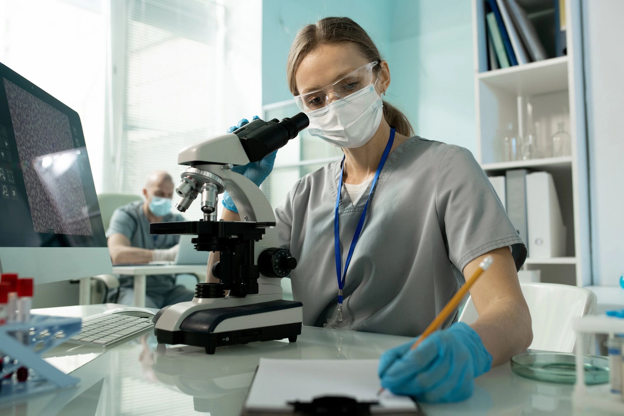 Lab professional making notes beside a microscope